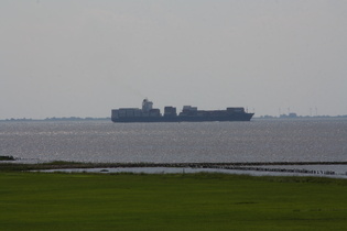 ein Containerfrachter in der Wesermündung, im Hintergrund Butjadingen